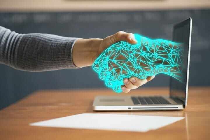 Human hand shaking digital hand emerging from laptop, symbolizing AI collaboration, technology assistance, and innovation.