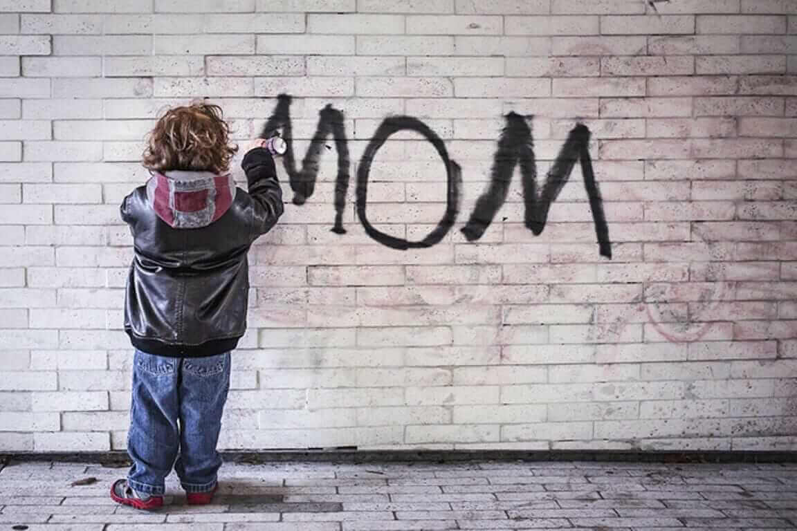 Child spray painting "MOM" on brick wall, graffiti art, urban creativity, street culture, playful expression, leather jacket.