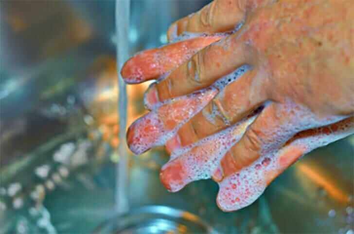 Hands covered in soap suds under running water, demonstrating proper hand washing technique for hygiene and cleanliness.