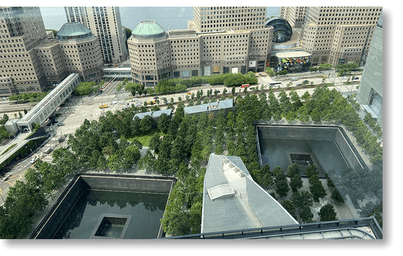 Aerial view of New York City 9/11 Memorial with reflecting pools, trees, and surrounding skyscrapers.