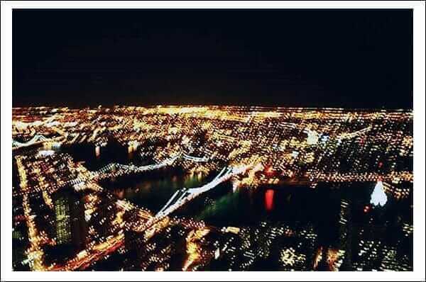 Nighttime cityscape with bright lights and bridges over water, showcasing urban skyline and vibrant nightlife.