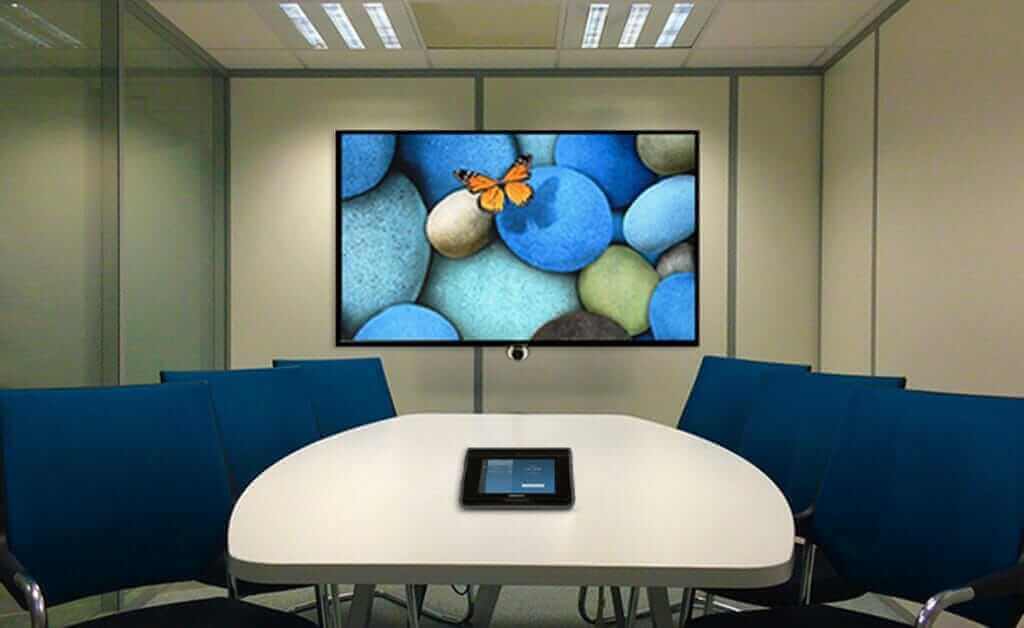 Modern conference room with video conferencing setup, large screen displaying colorful stones and butterfly.