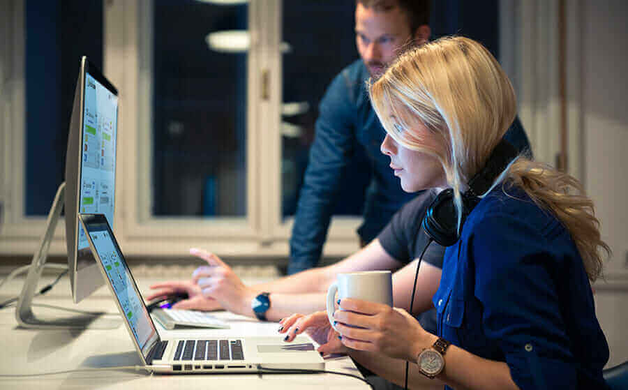 Team collaborating on computer screens in office, discussing data analytics and audio technology solutions.