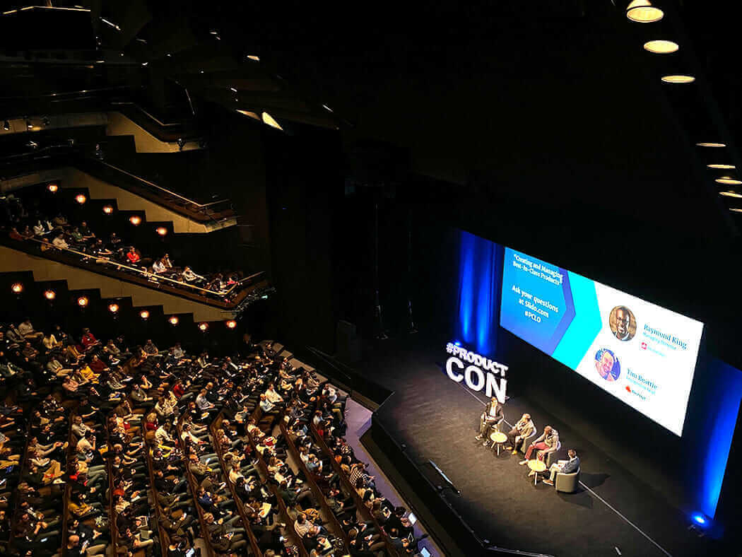 Large auditorium with audience attending AV broadcast event, featuring panel discussion on modern technology trends.