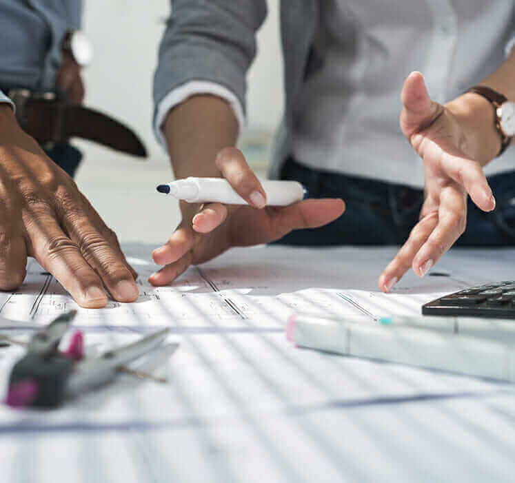 Engineering team collaborating on blueprints with pen and calculator, focusing on design and planning strategies.