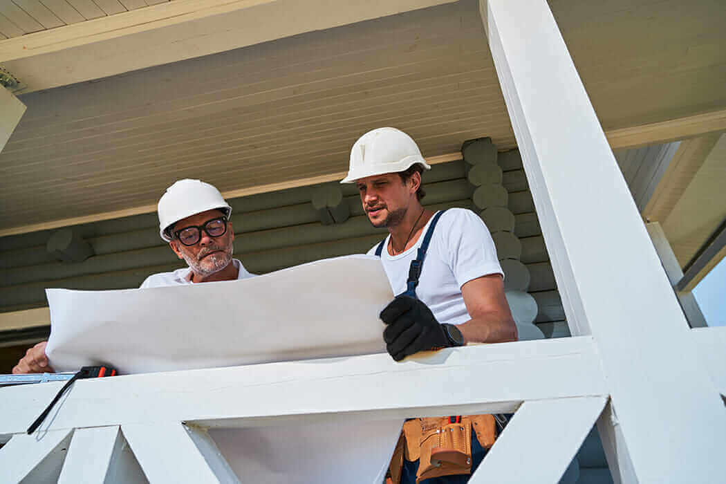 Engineer and construction worker reviewing house blueprint on site.