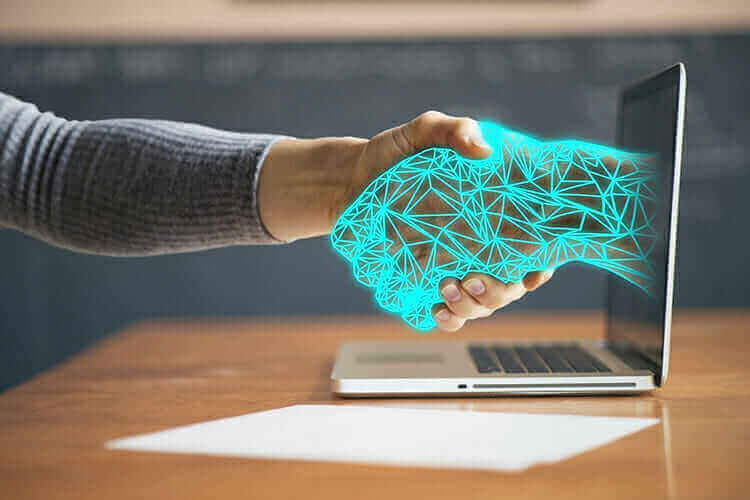 Handshake between human and digital hand emerging from laptop, symbolizing partnership with Captus Systems technology solutions.