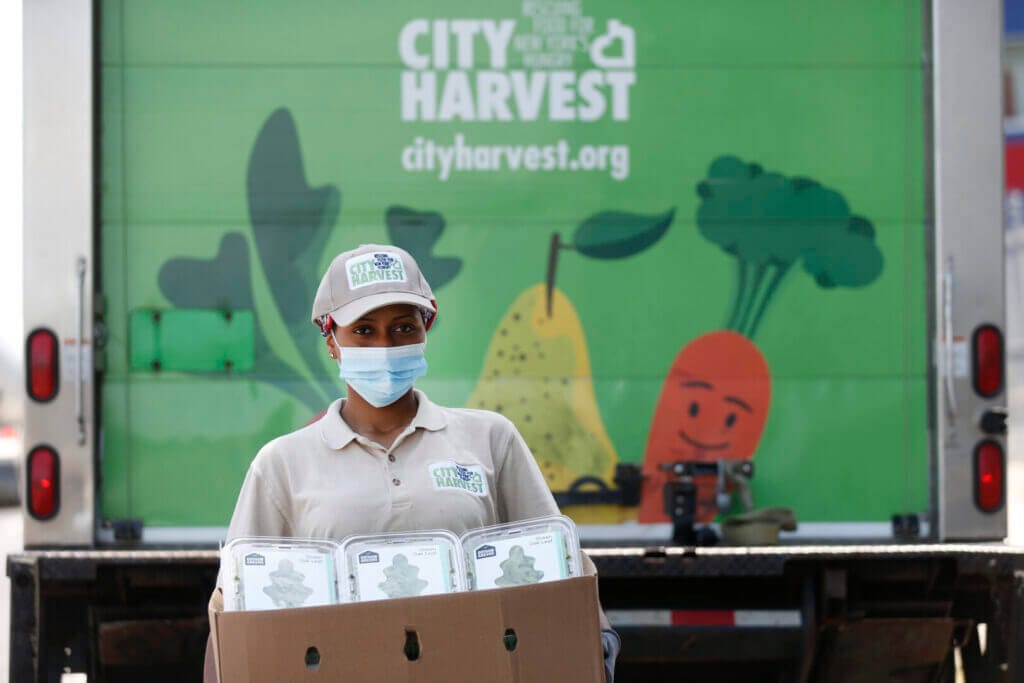 City Harvest worker delivers food boxes in front of branded truck, supporting hunger relief efforts.