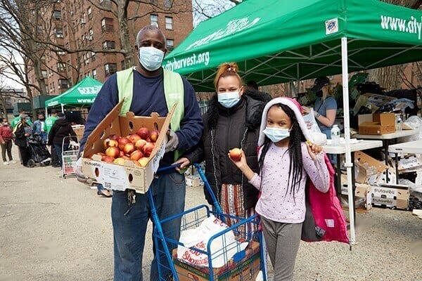 Community food distribution event with volunteers and families receiving fresh produce at outdoor market.