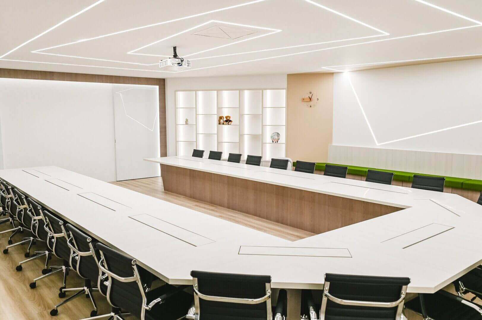 Modern conference room with white U-shaped table, black chairs, sleek lighting, and projector, ideal for meetings and presentations.
